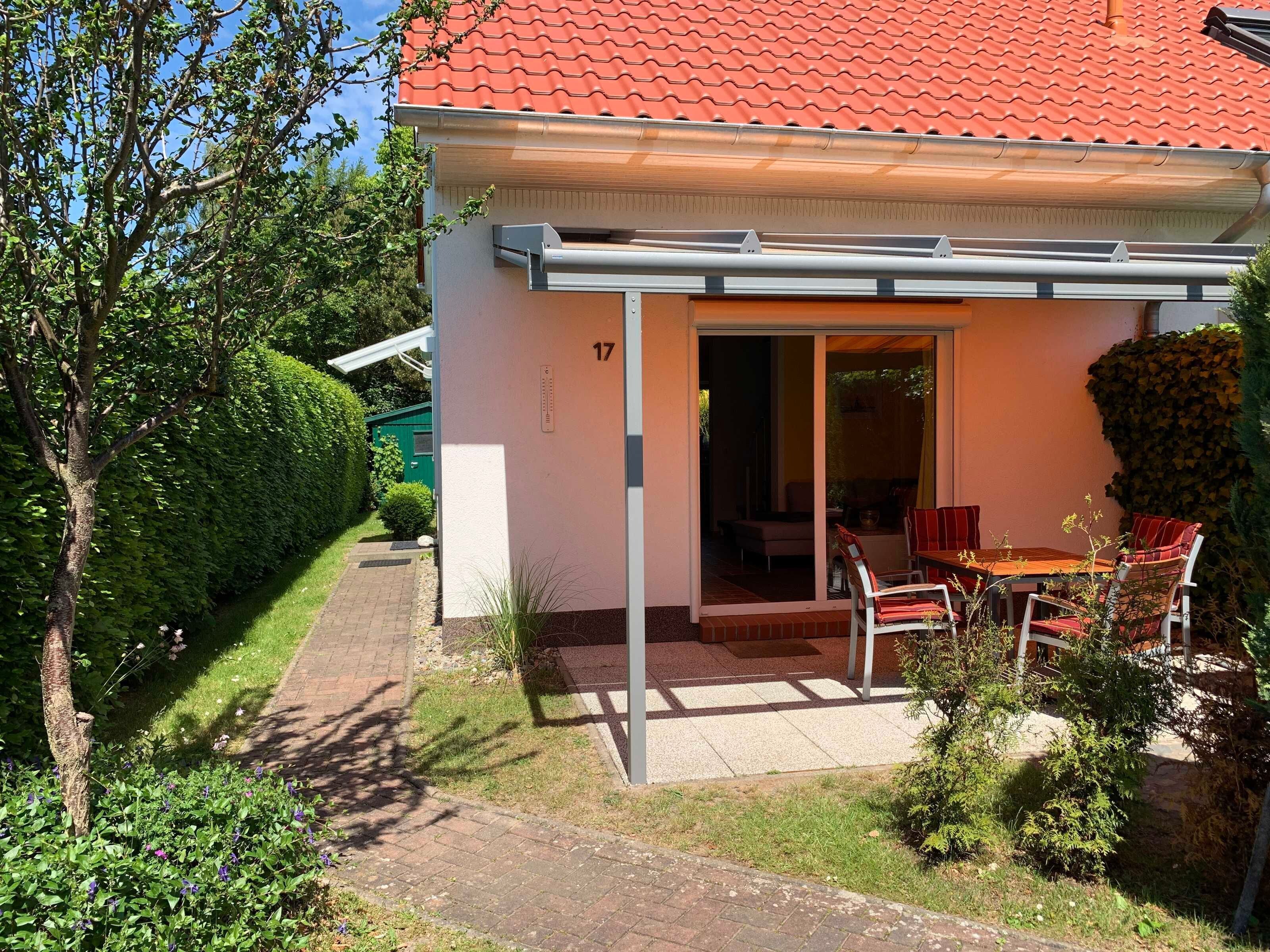 A house with a red tiled roof, a covered patio with a table and chairs, and a number 17 on the wall.