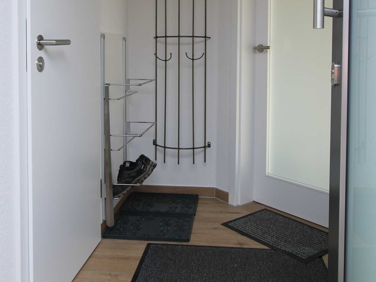 A hallway with a shoe rack, a door, and a doormat.