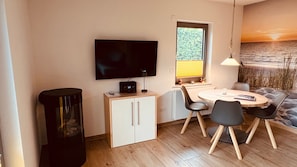 A compact room with a TV, a small cabinet, a table with chairs, and a window with a view of the beach. - Leuchtturmstraße house 17, only 100 m from the Baltic Sea - Leuchtturmstraße (Rerik)