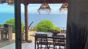 Une terrasse ouverte avec une table et des chaises, une vue sur l’océan et une pergola agrémentée de guirlandes lumineuses.