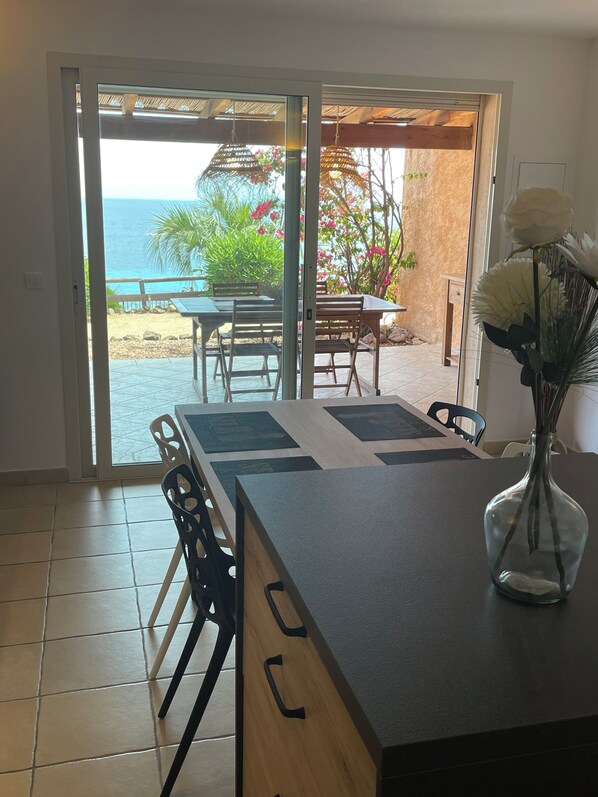 Et moderne køkken med en stor ø, et spiseområde med havudsigt og en skydedør til en udendørs terrasse.
