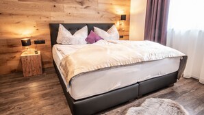 Une chambre moderne avec une tête de lit en bois, un lit doté d’un matelas gris et de draps blancs, deux lampes de chevet et un tapis en fourrure sur le sol.