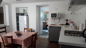 A compact kitchen with a refrigerator, microwave, and gas stove. There is a dining table with chairs and a small island with a sink. - Country house in country stone (Landrichamps)