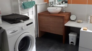 A modern bathroom with a washing machine, a sink, a mirror, and a small trash bin. - Country house in country stone (Landrichamps)