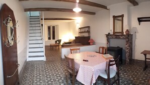 A dining area with a checkered tablecloth, wooden chairs, a fireplace, and a staircase leading to another room. - Country house in country stone (Landrichamps)