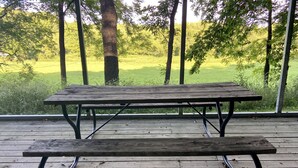 A wooden picnic table with metal legs on a wooden deck, overlooking a grassy field. - Trout Cove Cabin - Fish, Hike & Relax all in one setting just North of Decorah (Decorah)