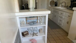 Een keuken met witte kasten, een aanrecht en planken met decoratieve objecten.