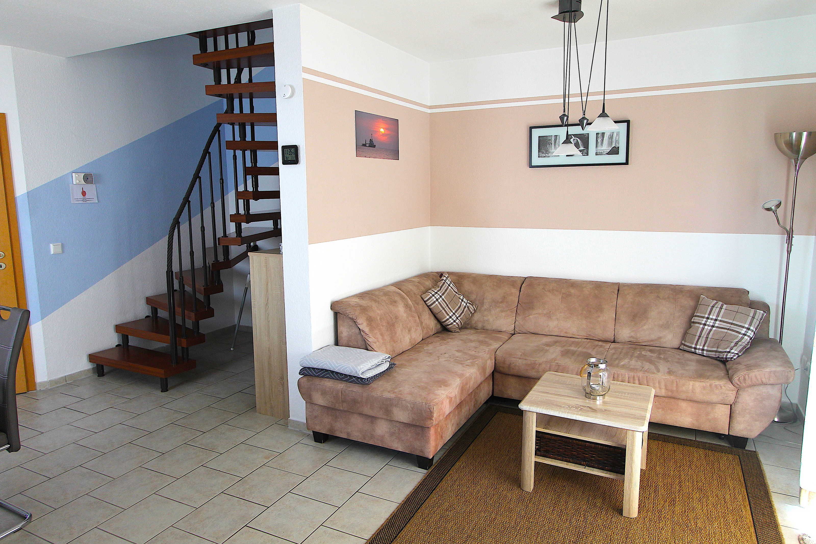 A living room with a brown sofa, a wooden coffee table, a staircase, and a wall-mounted picture.