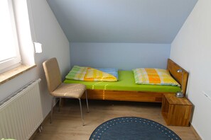 A small, single-bed room with a wooden headboard, a chair, a bedside table with a lamp, and a window with blinds. - Leuchtturmstraße house 15, only 150 m from the beach - Leuchtturmstraße 31 (Rerik)
