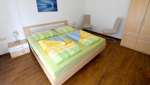 Un dormitorio ordenado con cama, una silla, armario y mesita de noche.