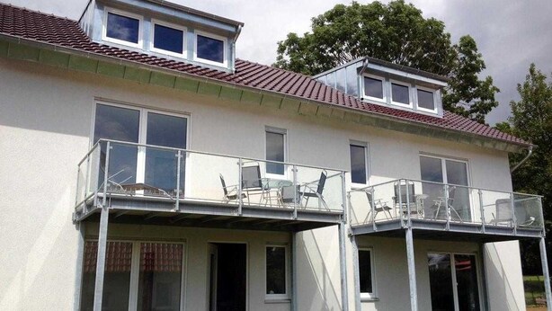 Un edificio de dos pisos con un balcón en la planta baja y un pequeño tragaluz en el ático.