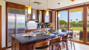 Cocina moderna con una isla grande, taburetes de bar, electrodomésticos de acero inoxidable y vistas al exterior.