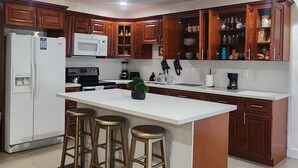 Une cuisine moderne avec des meubles en bois, un îlot central blanc doté de tabourets, un réfrigérateur, un four à micro-ondes et une machine à café.