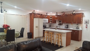 Une cuisine moderne avec des meubles en bois, un îlot central doté de tabourets, un coin repas avec une table et des chaises, et un lustre.