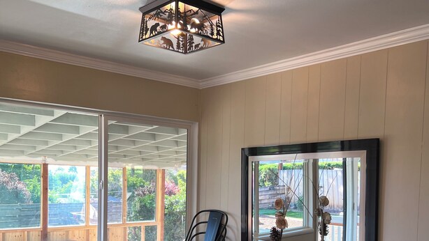 A dining area with a table set for four, a chandelier, and large windows offering a view of the outdoors.