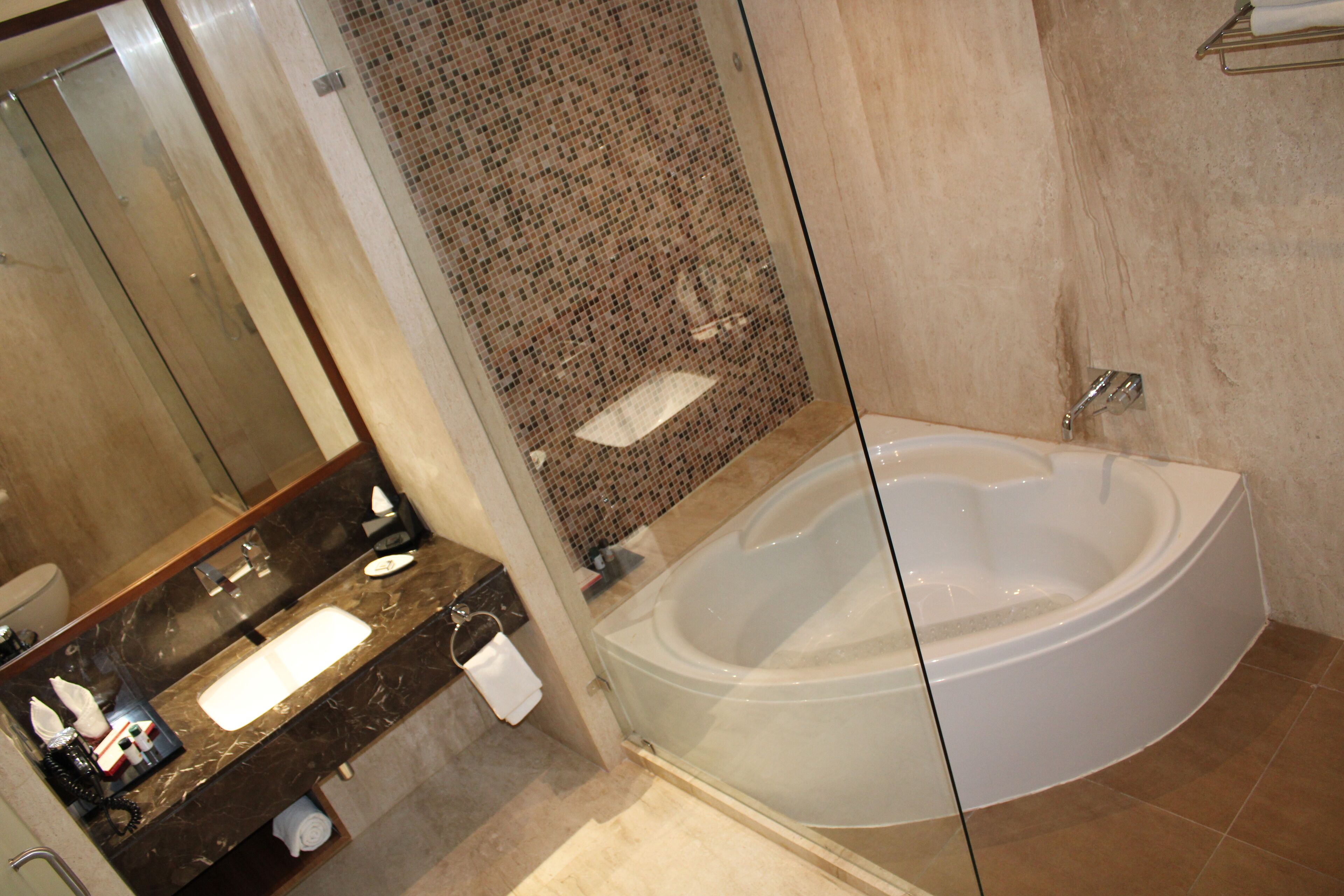 Een moderne badkamer met een glazen jacuzzi, een marmeren wastafel en een grote spiegel.
