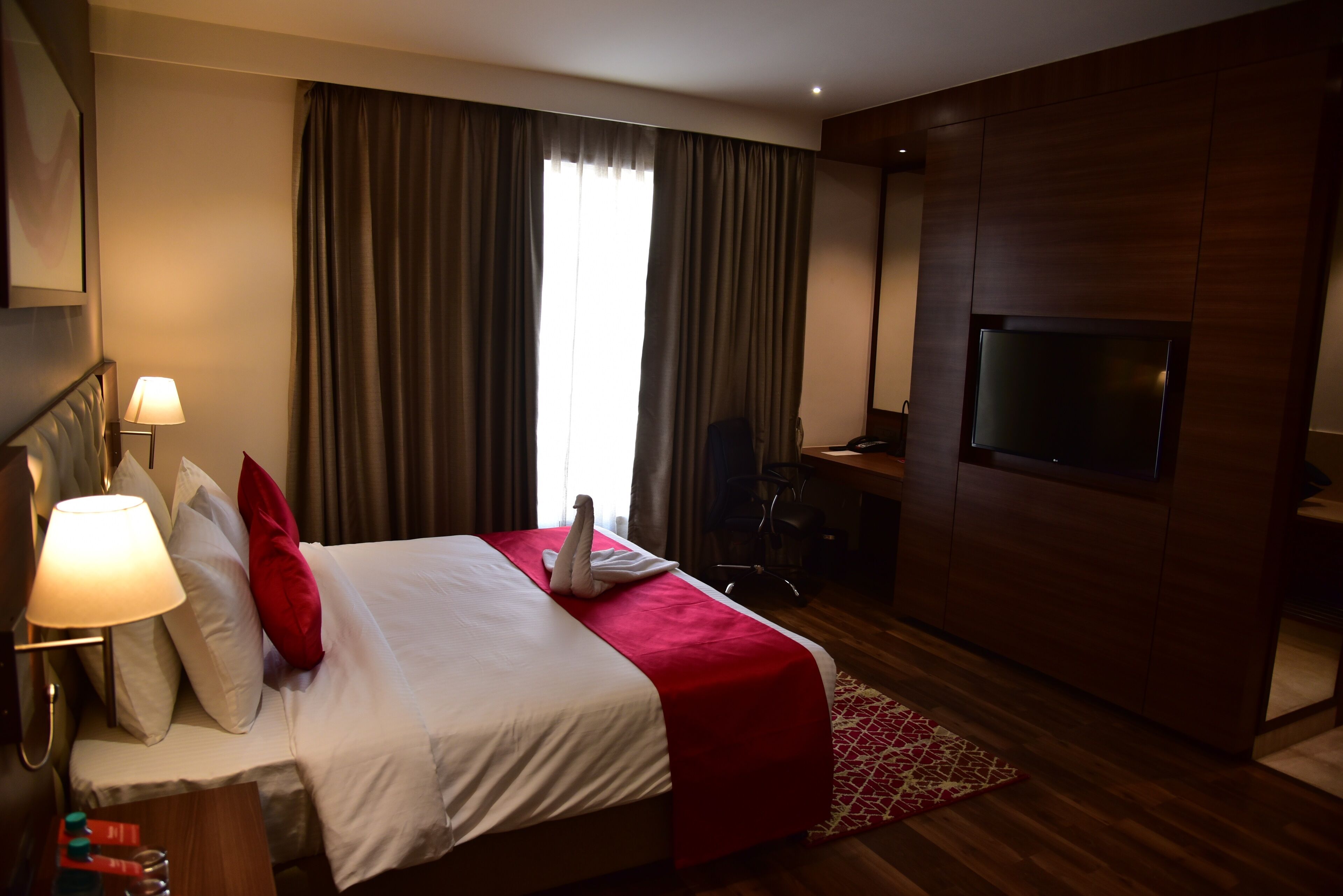 Habitació d'hotel amb llit, escriptori, televisió i làmpada.