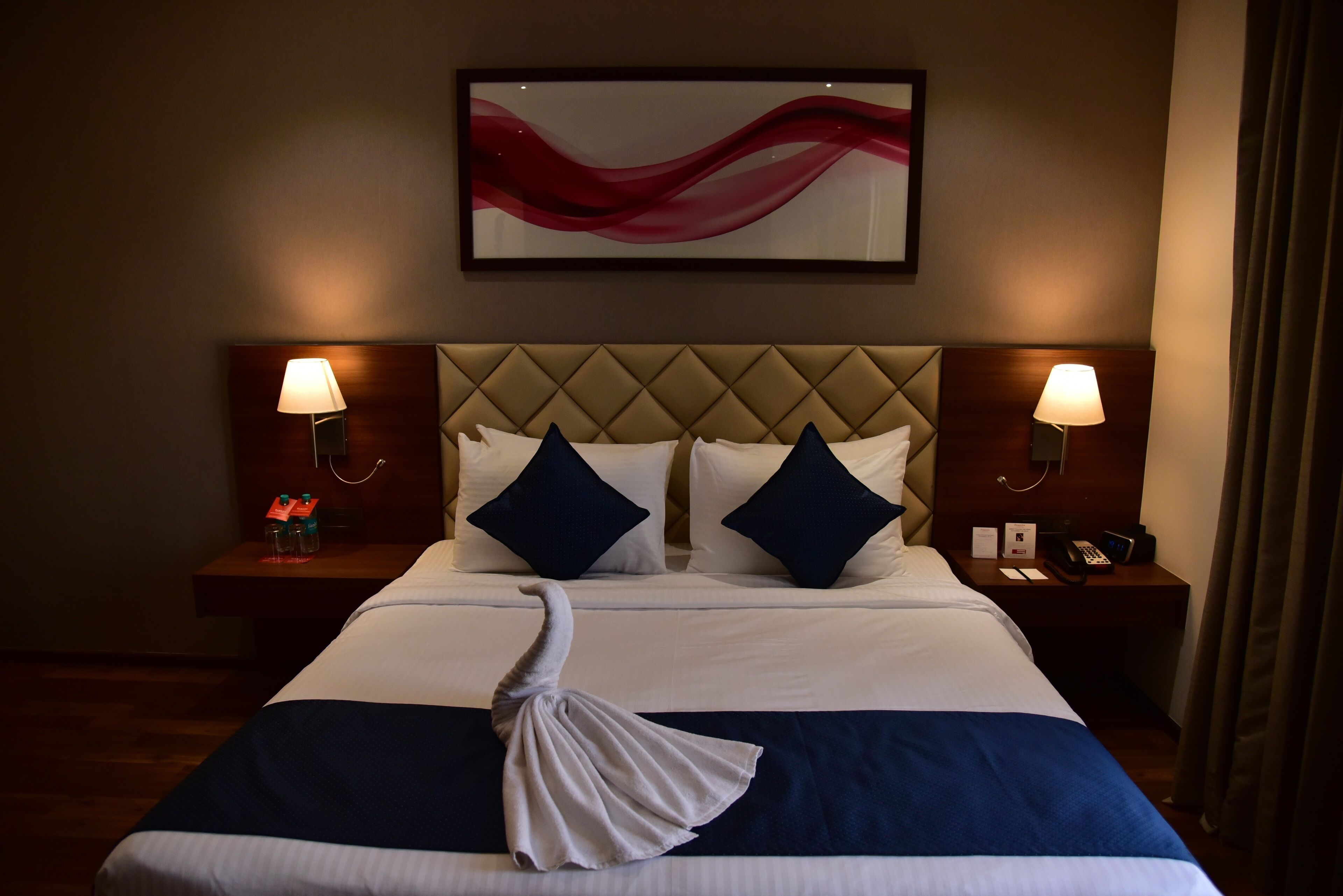 A hotel room with a large bed, two bedside tables, a headboard, and a wall-mounted artwork.