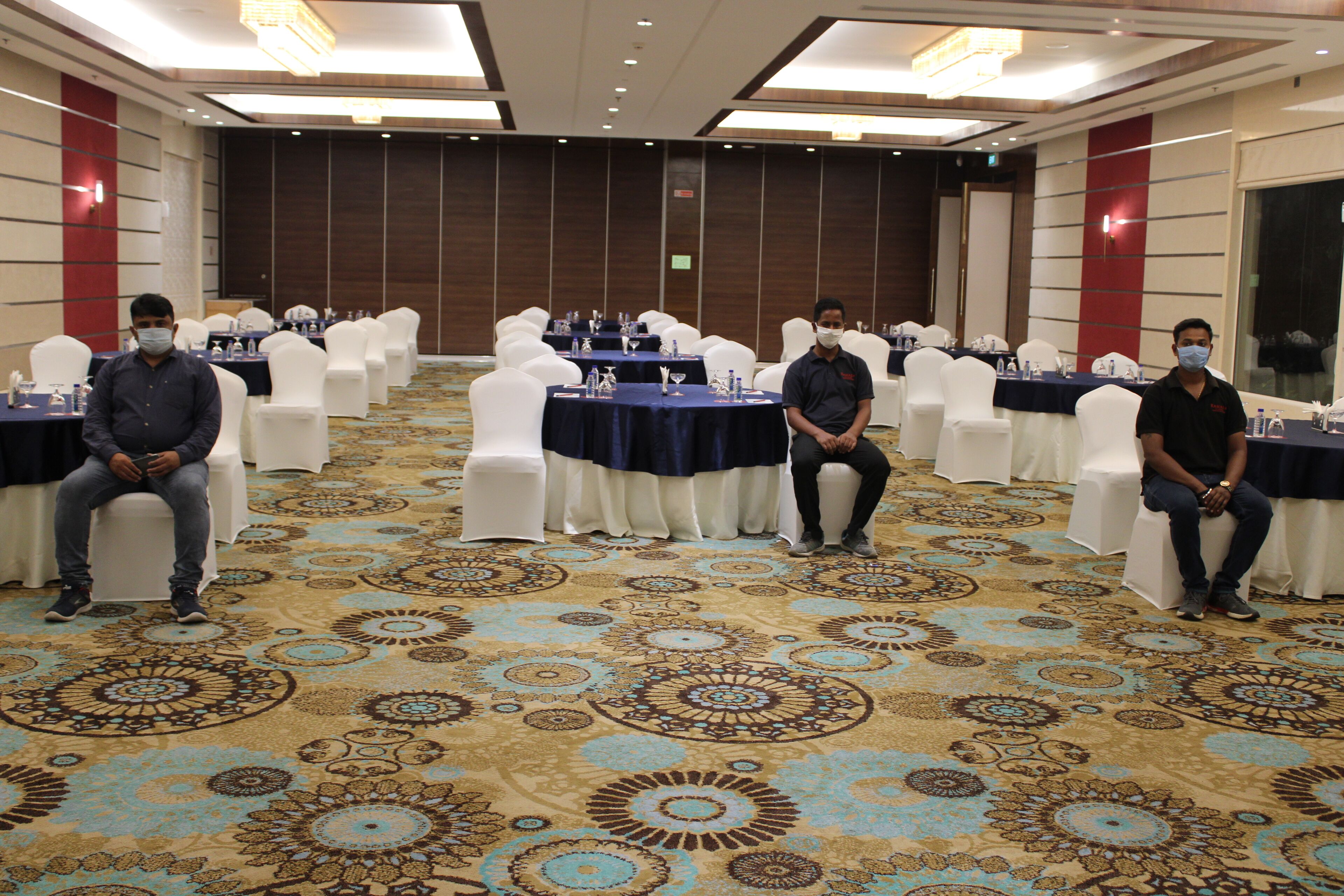 A conference room with round tables, white chairs, and a patterned carpet.