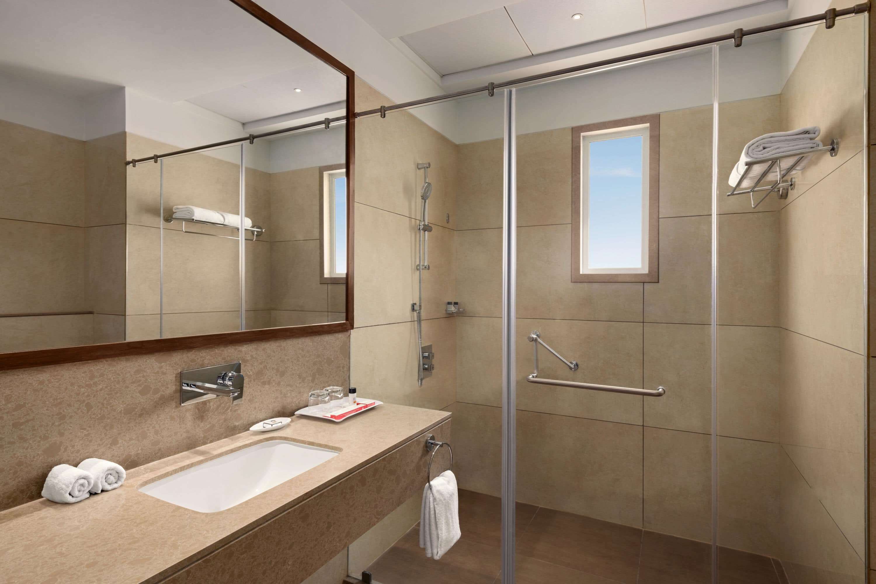 A modern bathroom with a large mirror, a sink, a shower with a glass door, and a towel rack.