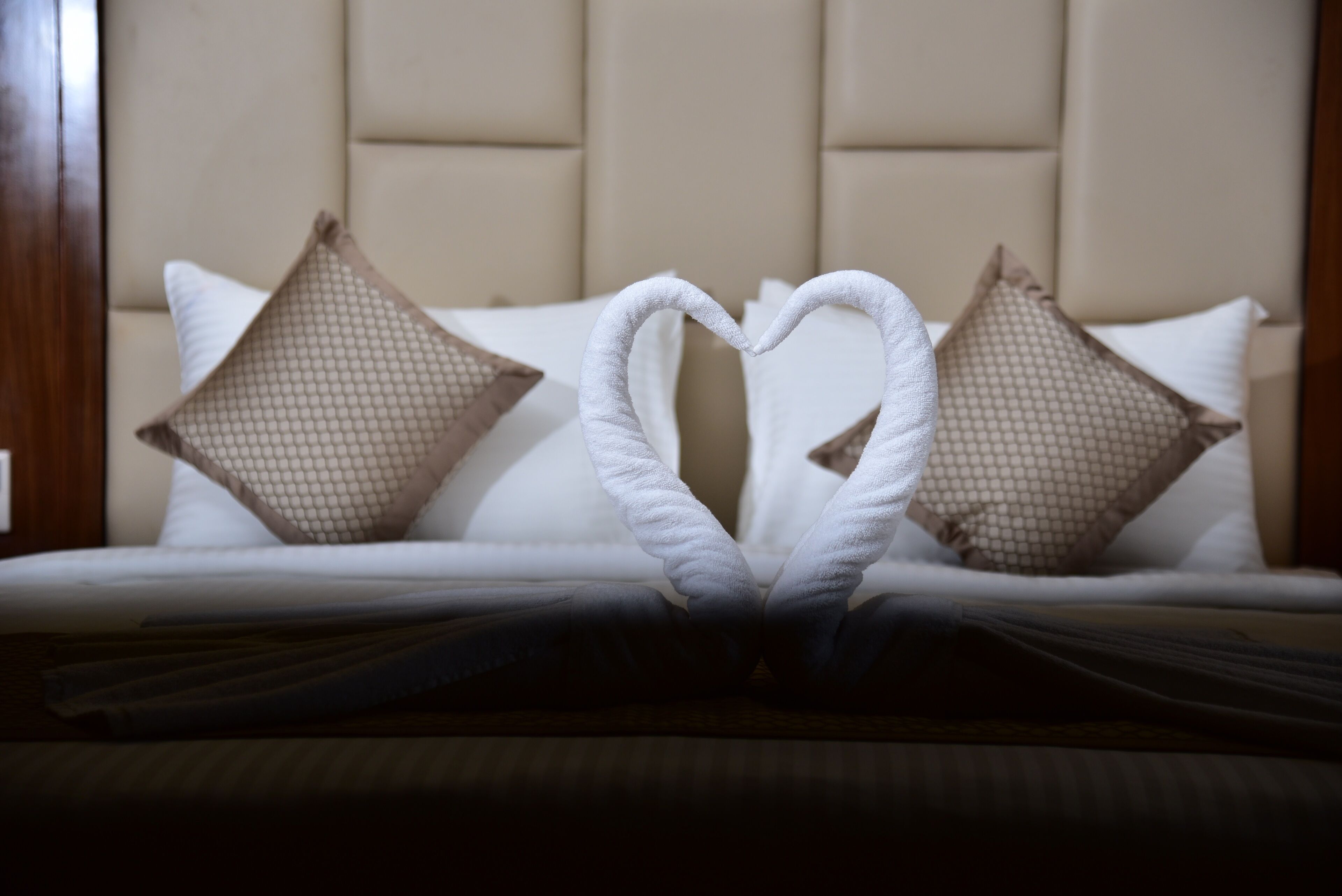 Un letto con un asciugamano disposto a forma di cuore e due cuscini decorativi.