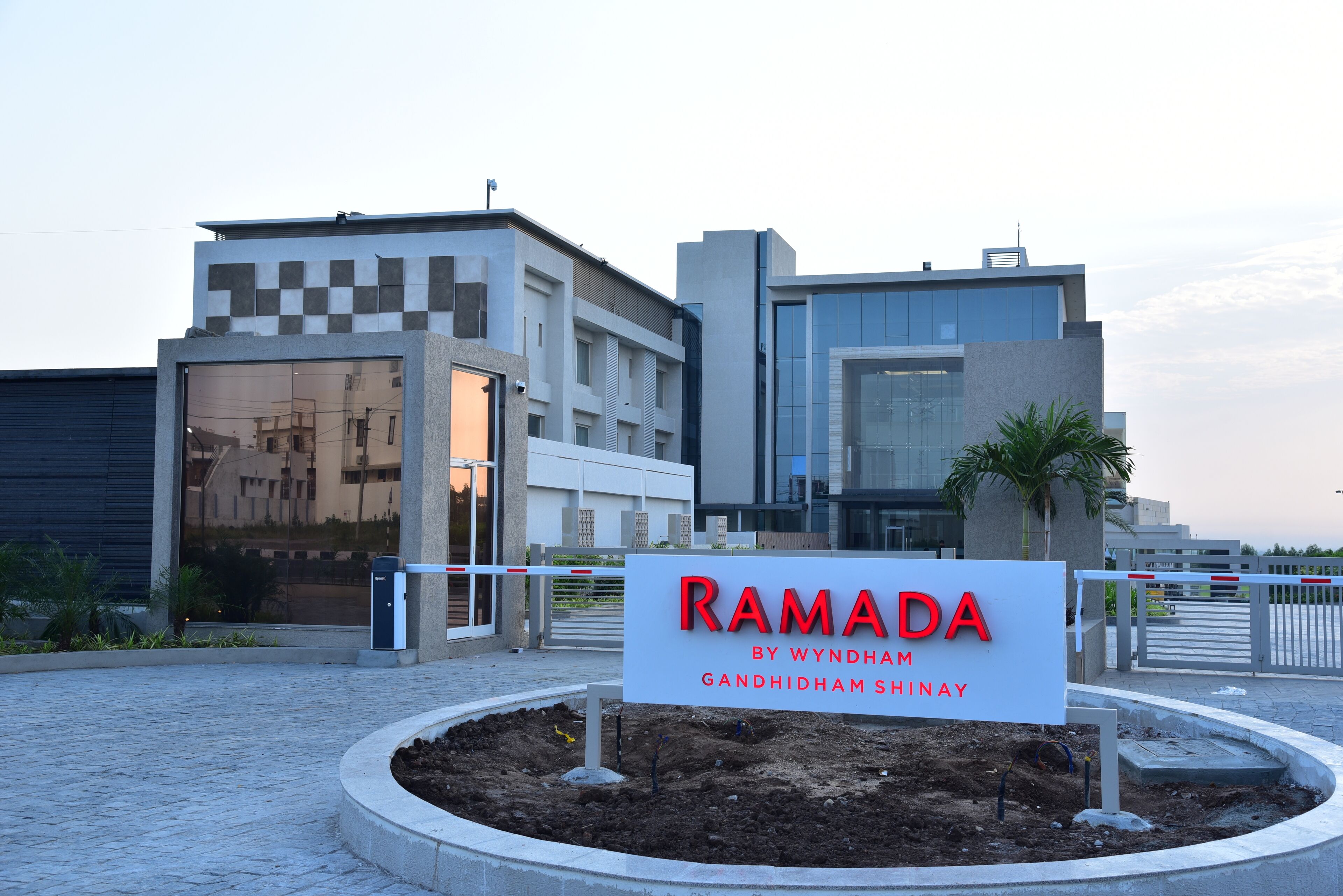 A modern building with a sign reading "RAMADA BY WYNDHAM GANDHIDHAM SHINAY".