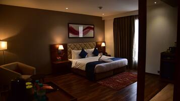 A hotel room with a bed, two bedside tables, a chair, a coffee table, and a red patterned rug.