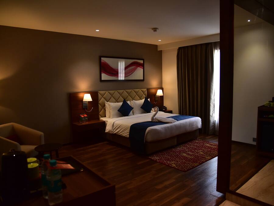 A hotel room with a bed, two bedside tables, a chair, a coffee table, and a red patterned rug.