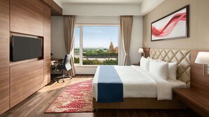 Ein modernes Hotelzimmer mit einem großen Bett, einem Fernseher, einem Schreibtisch und Blick auf die Stadt.