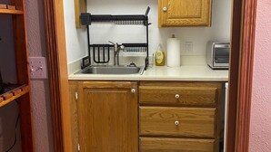 Cocina compacta con armarios de madera, un fregadero, un escurreplatos, un tostador y una encimera.