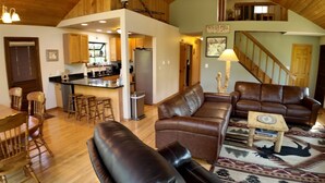 A spacious living area with leather sofas, a dining table with chairs, and a kitchen area with wooden cabinets and a refrigerator.