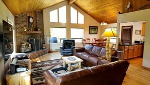 A cozy living room with a fireplace, leather furniture, and large windows.