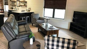 Ein modernes Wohnzimmer mit einem Ledersofa, einem karierten Sessel, einem Couchtisch und einem Essbereich mit Küchenzeile.
