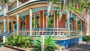A historic building with a covered porch, multiple windows, and hanging plants. - Heated Pool Access | 5*Clean | Flex Cancelation (Savannah)