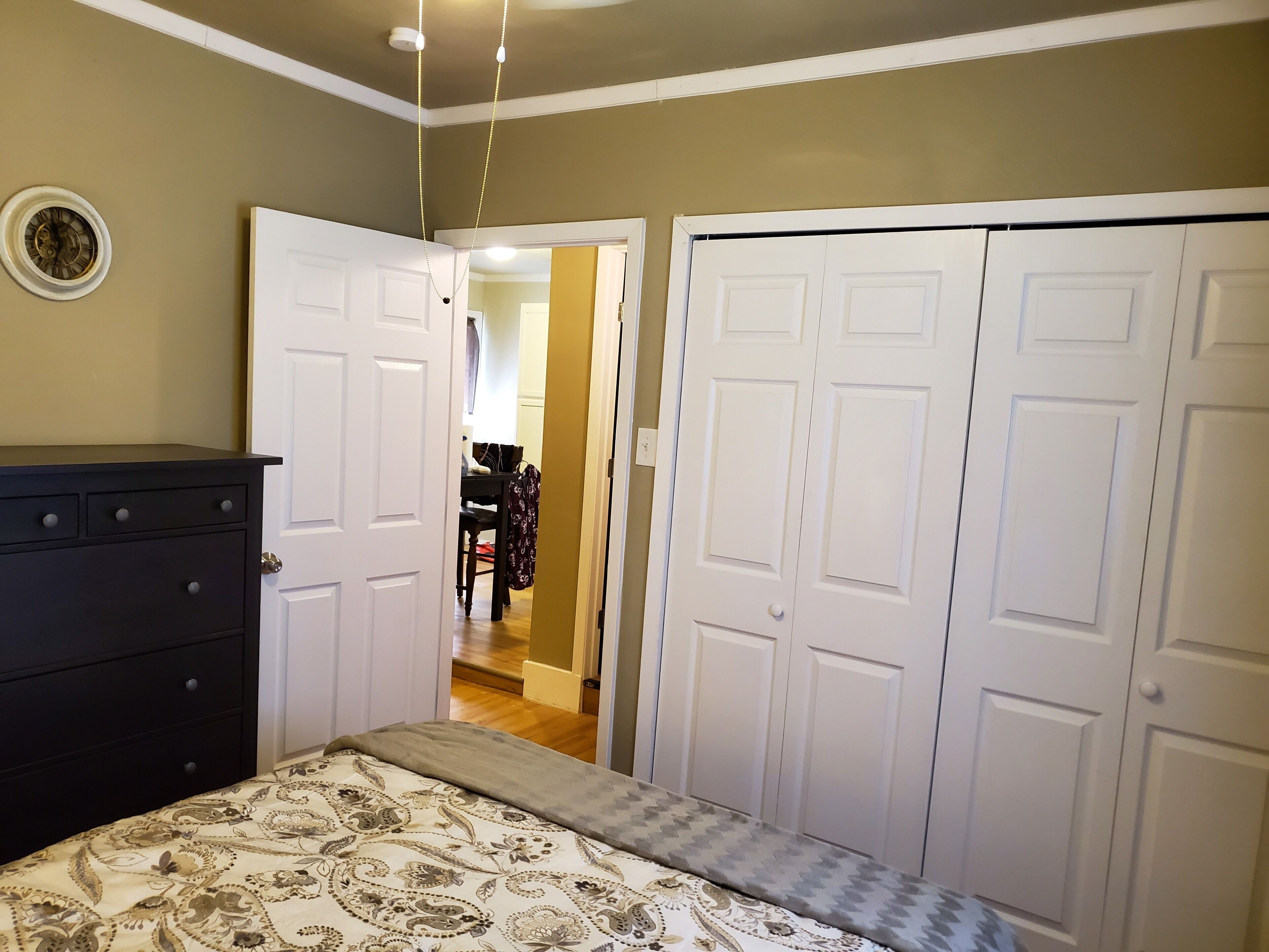 Une chambre à coucher comprenant un lit, une commode et deux portes blanches donnant sur d’autres pièces.