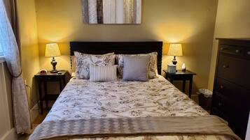 A neatly made bed with patterned bedding, two bedside lamps, a clock, and a wall-mounted artwork.