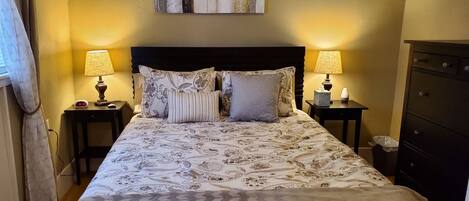 A neatly made bed with patterned bedding, two bedside lamps, a clock, and a wall-mounted artwork.