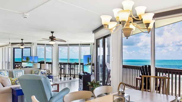 Un vaste espace de vie doté d’une grande fenêtre donnant sur l’océan, d’une table à manger et d’un ventilateur de plafond.