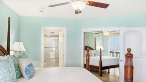Une chambre avec un grand lit, un ventilateur de plafond et une porte donnant sur une autre pièce.