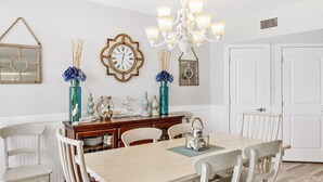 Une salle à manger avec une table en bois, des chaises blanches, un lustre et des objets décoratifs accrochés au mur.