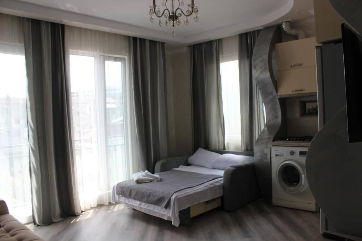 A modern bedroom with a bed, a washing machine, and a view of the city.