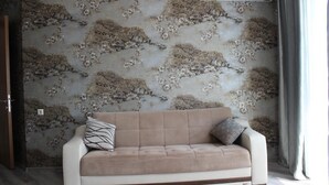 Una sala de estar con un sofá color beige, papel tapiz estampado y un equipo de aire acondicionado.