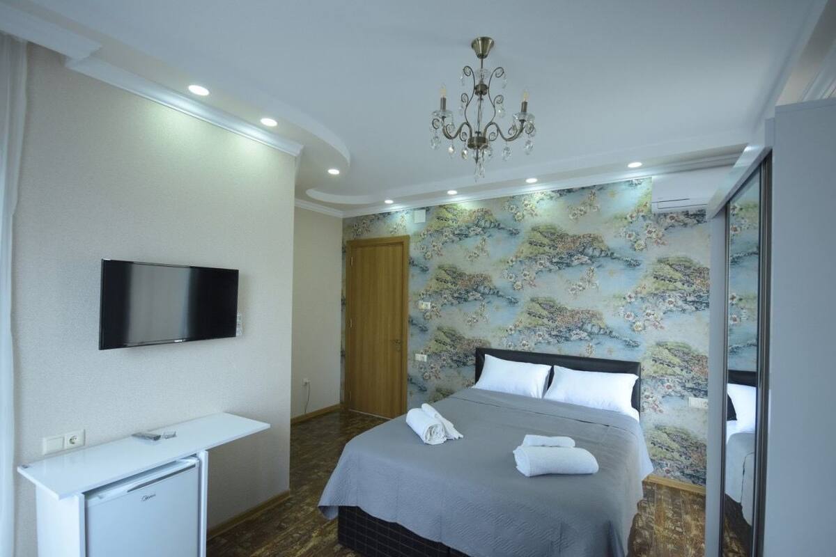 A hotel room with a bed, a TV, a desk, and a chandelier.