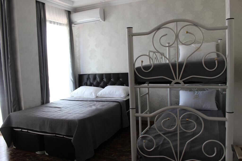 A hotel room with a single bed, a bunk bed, a grey upholstered headboard, and a window with curtains.