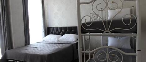 A hotel room with a single bed, a bunk bed, a grey upholstered headboard, and a window with curtains.