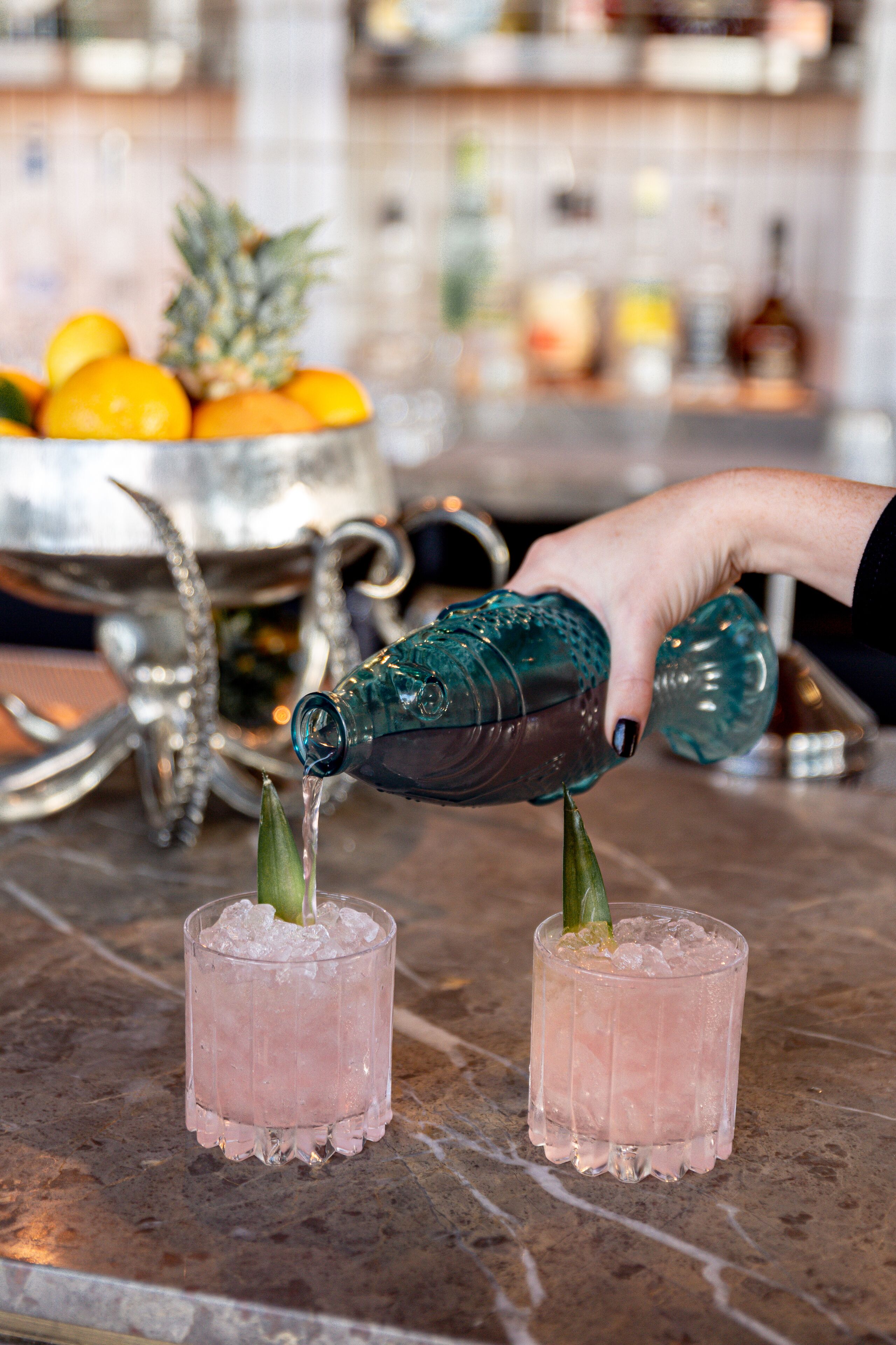 A hand pouring a drink into a glass with a pineapple garnish.