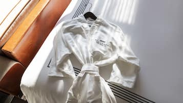 Un kimono de artes marciales blanco colgado de un perchero negro, con un banco de madera y una pared blanca al fondo.