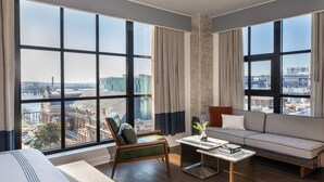 Una habitación de hotel moderna con ventanas amplias, un sofá, una silla y una mesita de café.