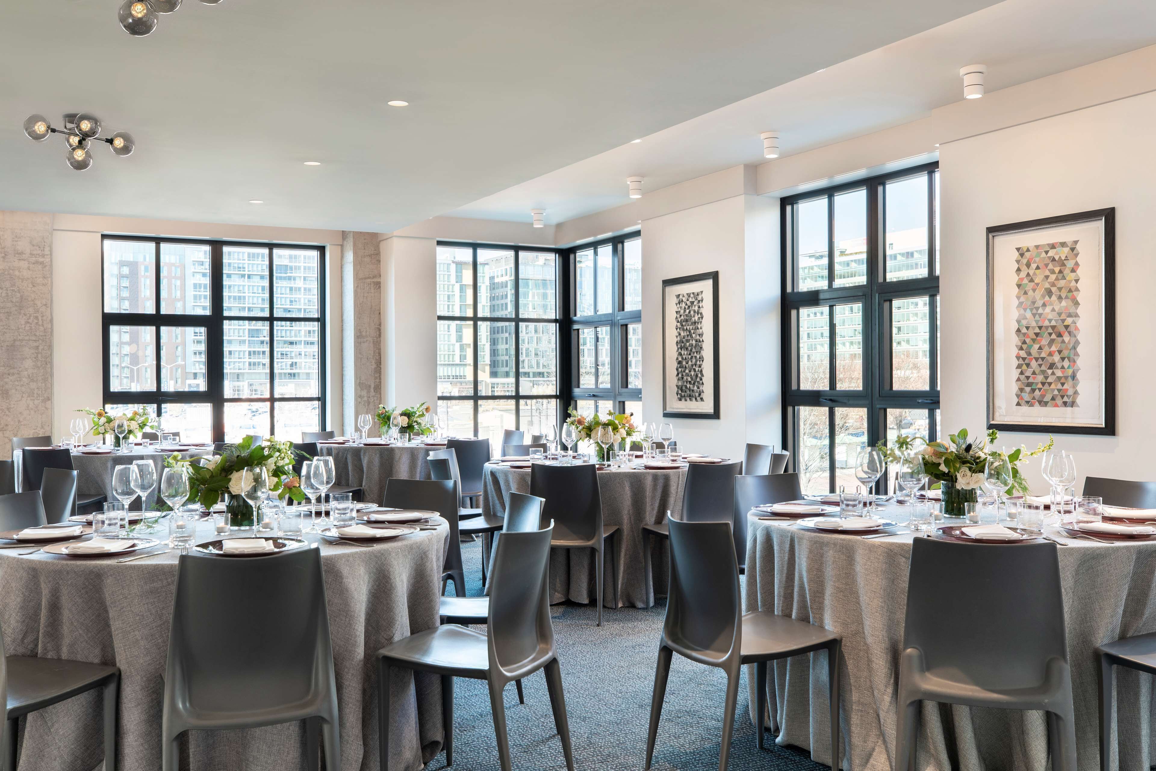 Un salón de conferencias con varias mesas dispuestas para comer, amplias ventanas con vistas a la ciudad e iluminación moderna.