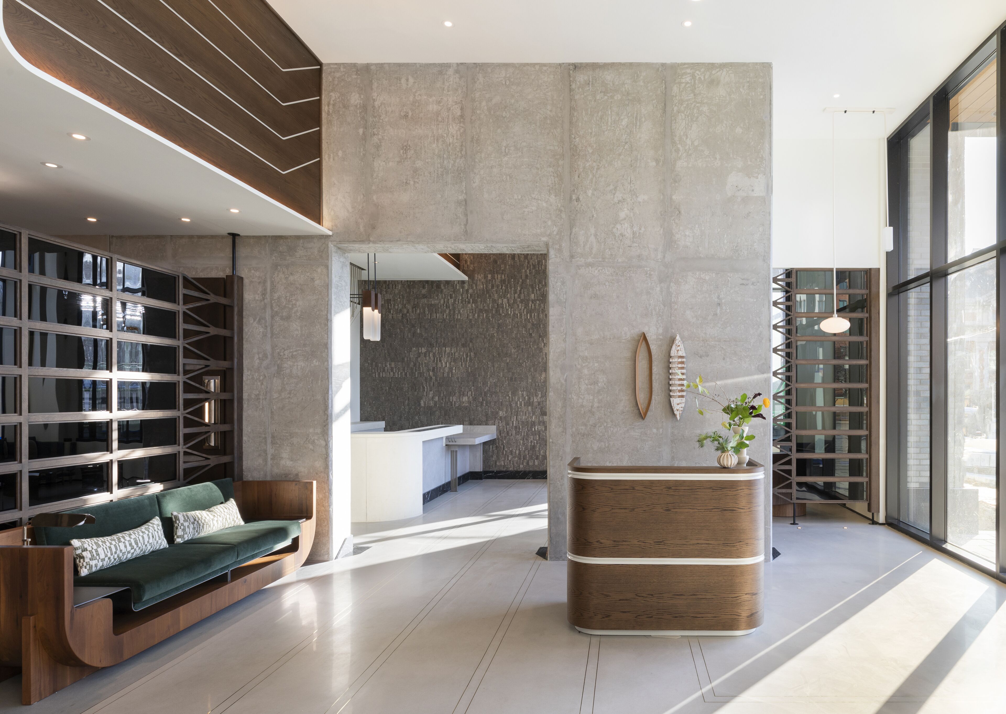 A modern lobby with a wooden reception desk, a green sofa, and a large window offering a view of the outside.